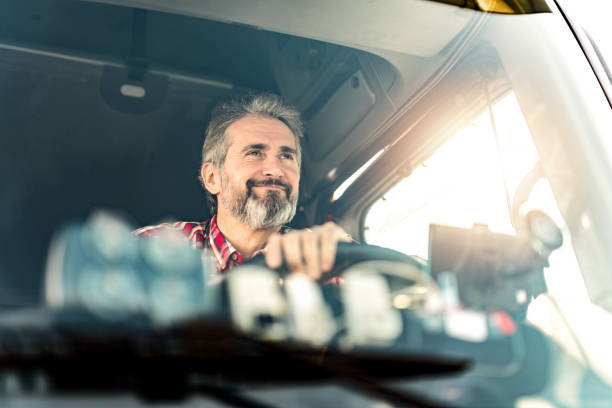 Front view of truck driver sitting in his truck and driving to a warehouse.